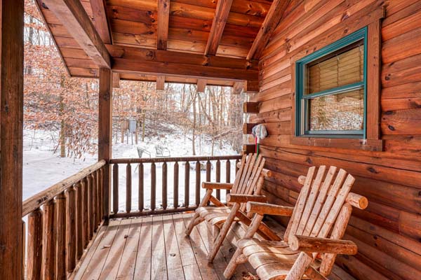 Two wood chairs on the porch looking out to snowy woods
