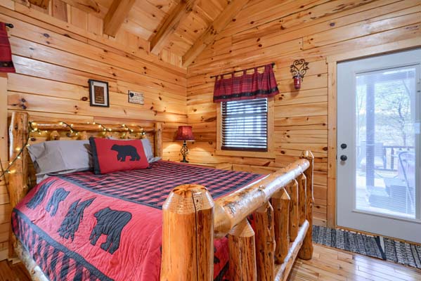 Queen log bed with red and black quilt beside the patio door