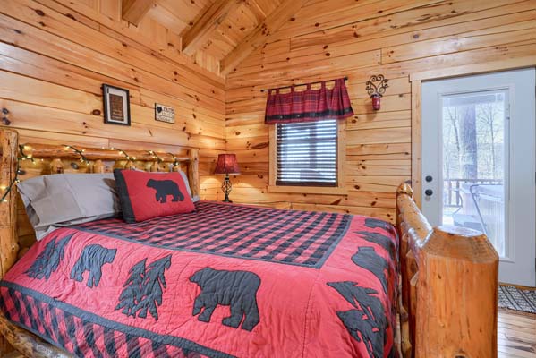 Queen log bed beside a window with a red shade