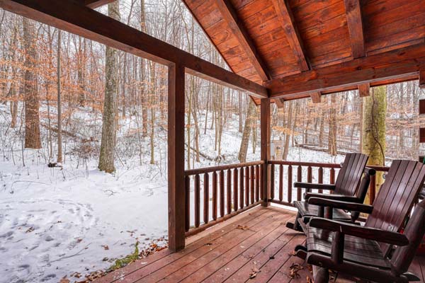 Covered porch with two rocking chairs facing snowy woods