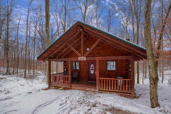 Snow covered ground leading to the small log cabin