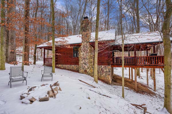 Fire pit with two snow covered chairs and the cabin behind